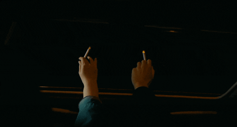 Gif of a scene where two people hold their cigarettes outside the sunroof of a car from the film Drive My Car